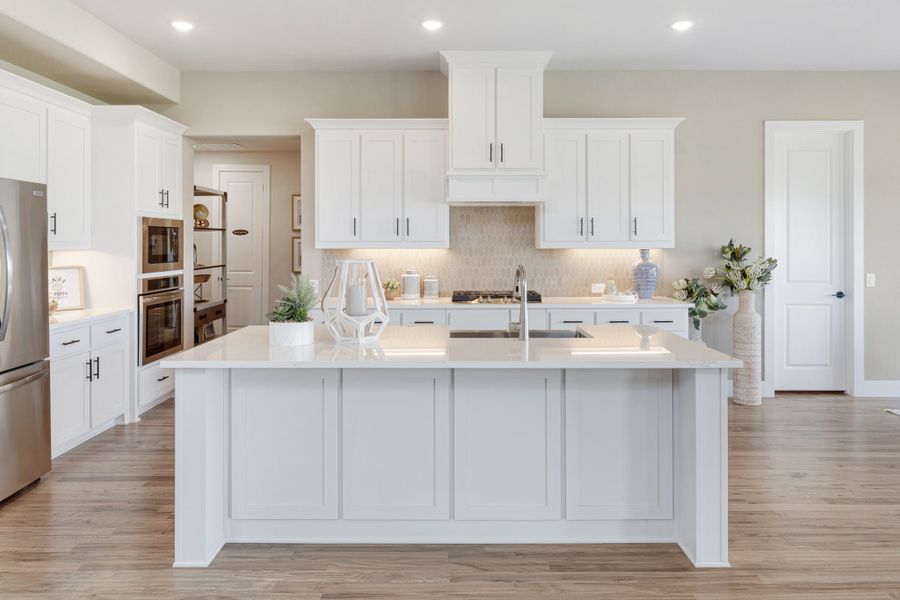 Kitchen with large white island, white shaker cabinets, quartz countertops, and light wood floors
