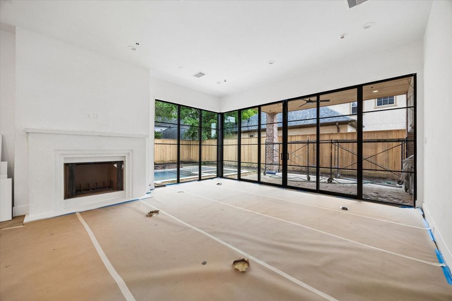 Bright, open-concept living room with sliding doors and expansive corner windows that seamlessly connect to the outdoor living space. Covered outdoor kitchen to included gas grill and beverage refrigerator. Pictured April 2026.