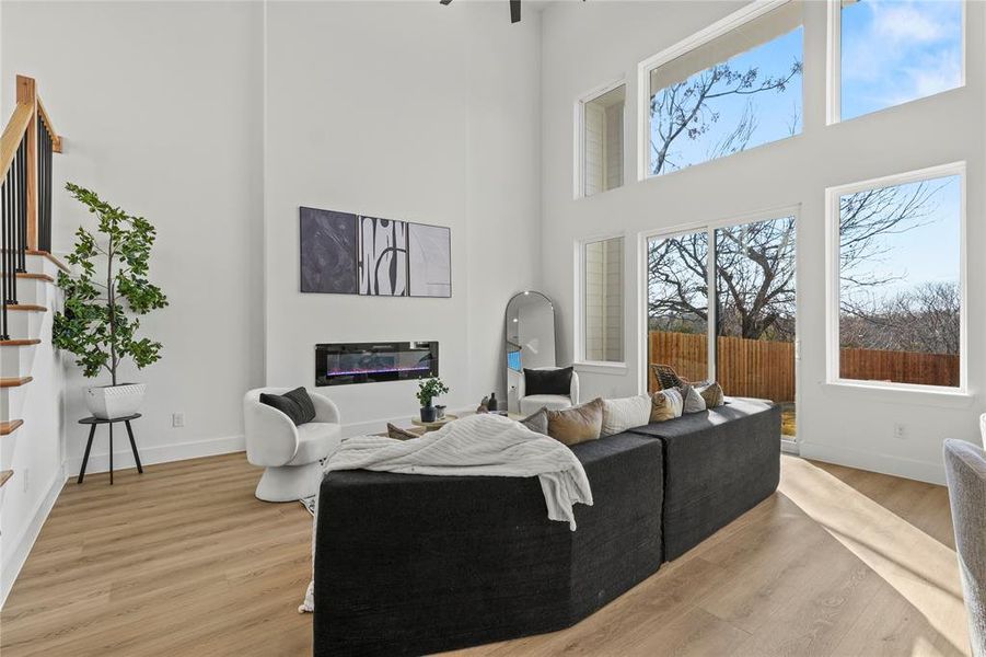 Living room with a glass covered fireplace, light wood finished floors, and a high ceiling
