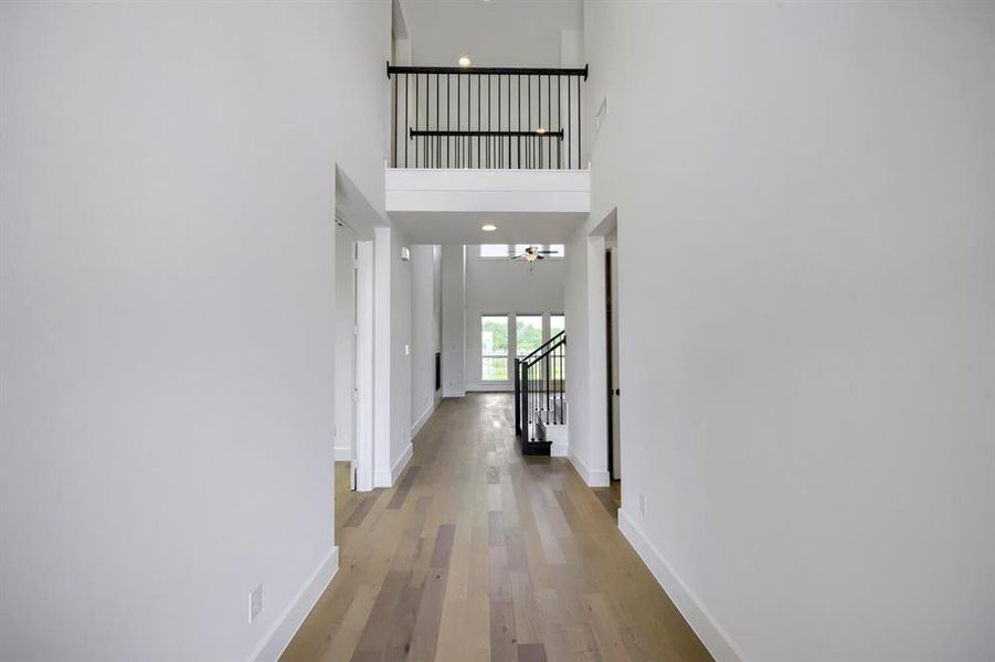 Two-story foyer featuring light wood-finish flooring, white walls, and a black metal spindle railing Two-story foyer featuring light wood-finish flooring, white walls, and a black metal spindle railing
