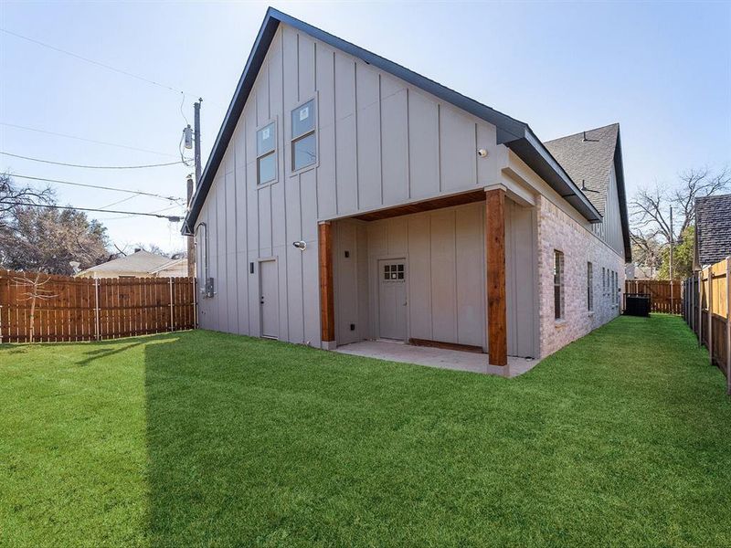 Rear view of house with a fenced backyard, brick siding, a yard, board and batten siding, and a patio area