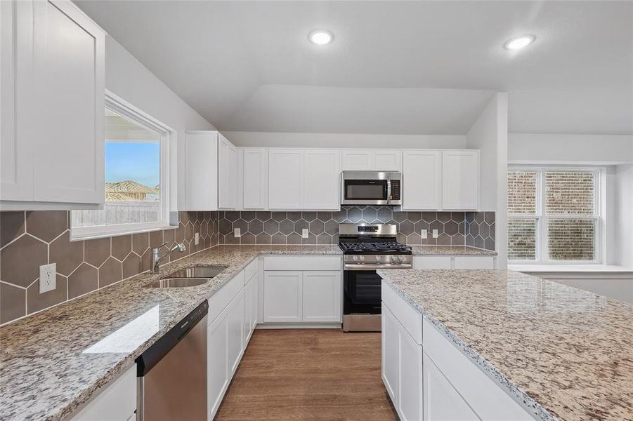 Kitchen with a sink, light stone countertops, wood finished floors, stainless steel appliances, and white cabinets Kitchen with a sink, light stone countertops, wood finished floors, stainless steel appliances, and white cabinets