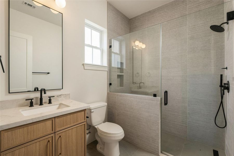 This secondary bath pairs Mount Blanc Quartzite with full-height designer tile and a frameless glass shower, creating a polished ensuite experience with finishes typically reserved for a primary suite.