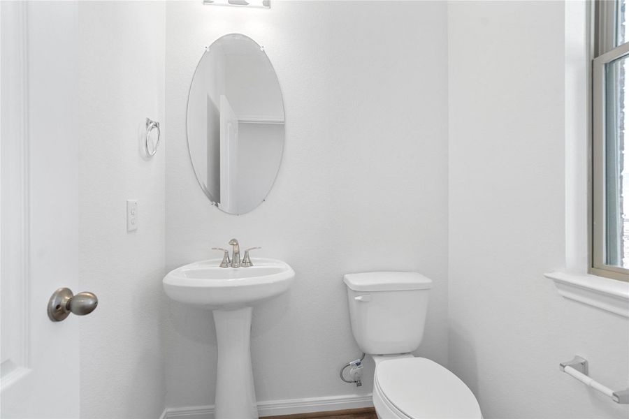 The powder bathroom features vinyl plank flooring, custom paint, pedestal sink with Moen faucet, and oval mirror.