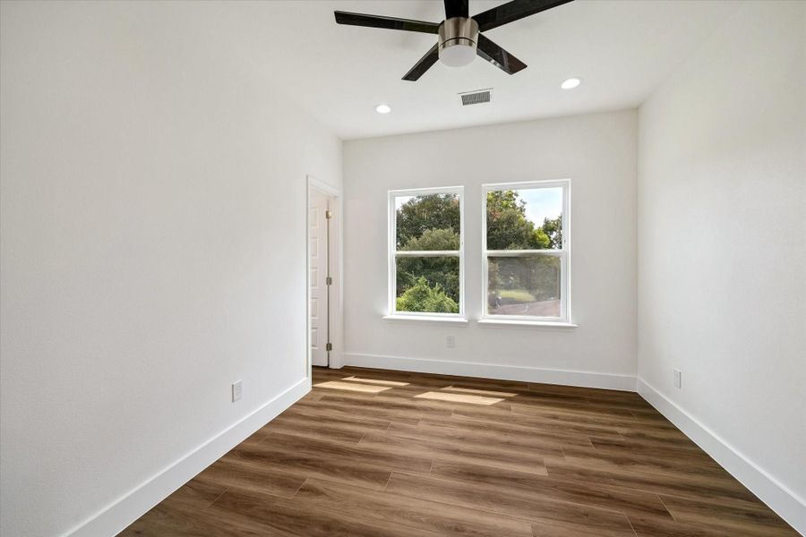 Peaceful and light-filled, this bedroom features warm wood-look flooring, crisp white walls, and two large windows framing leafy outdoor views. A modern ceiling fan adds comfort and contemporary style, while recessed lighting keeps the room bright after sunset. The simple, neutral palette provides an easy backdrop for a variety of furnishings and décor. Generous wall space and abundant daylight create a calm, flexible retreat with the fresh, move-in-ready feel carried throughout the home. Peaceful and light-filled, this bedroom features warm wood-look flooring, crisp white walls, and two large windows framing leafy outdoor views. A modern ceiling fan adds comfort and contemporary style, while recessed lighting keeps the room bright after sunset. The simple, neutral palette provides an easy backdrop for a variety of furnishings and décor. Generous wall space and abundant daylight create a calm, flexible retreat with the fresh, move-in-ready feel carried throughout the home.