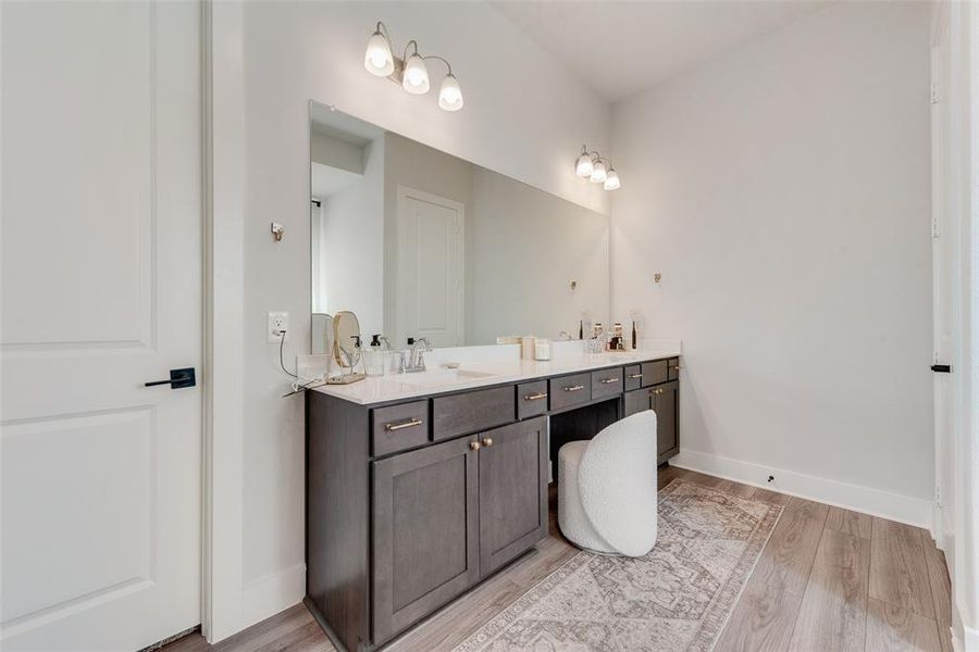 Spacious bathroom vanity featuring a light-colored countertop, dual sinks, extensive storage cabinetry, and a dedicated vanity seating area