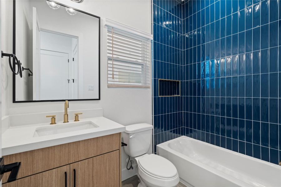 Attached secondary bedroom with darker tone designer tilework, European-style white oak cabinetry, white quartz countertops, and elegant champagne bronze Delta shower fixtures — blending style and function throughout every bath in the home.