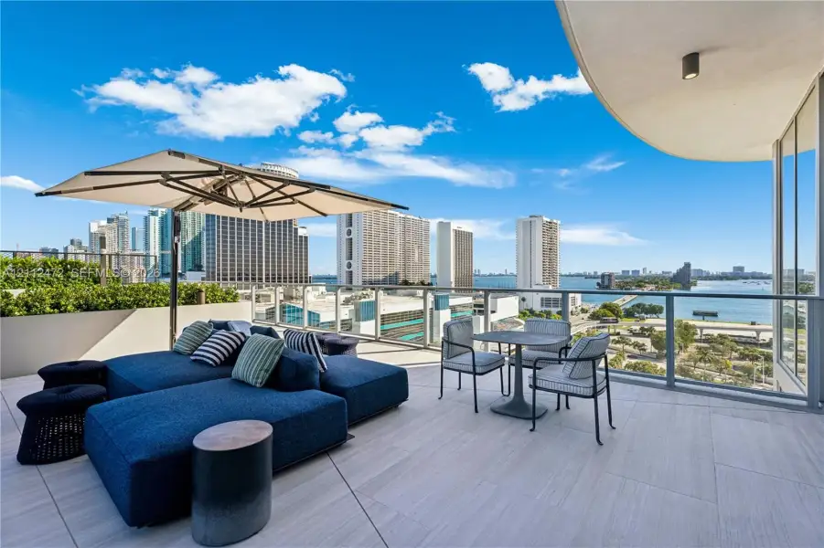 Expansive outdoor terrace featuring light-toned tile flooring, glass panel railings, and recessed ceiling lighting