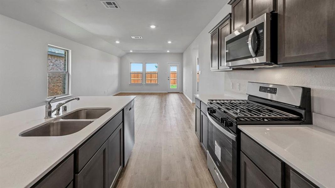 Kitchen featuring dark wood-finish cabinetry, light-toned countertops, stainless steel appliances, and a dual basin sink