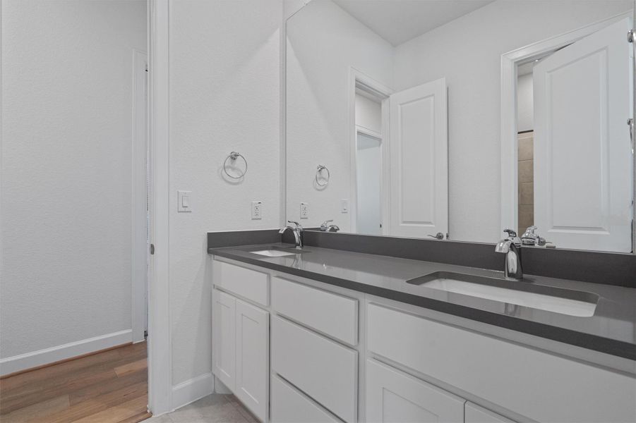 Double vanity with integrated sinks and dark countertop, chrome fixtures, white cabinetry, and large wall-mounted mirror