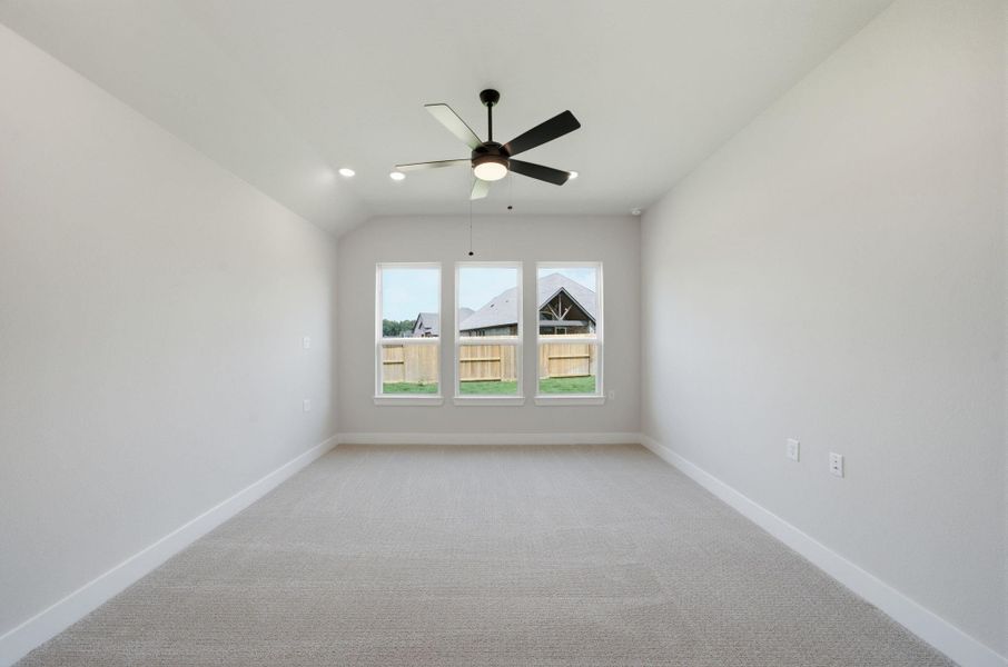Spacious owner’s suite with a vaulted ceiling, ceiling fan, recessed lighting, and three windows providing abundant natural light.