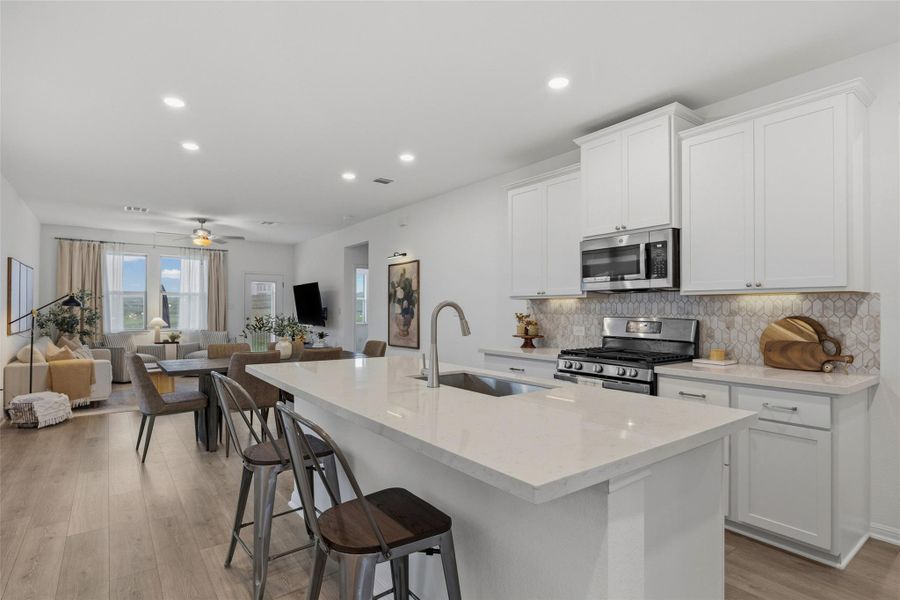 Open-concept kitchen featuring a large island with sink, white shaker cabinetry, stainless steel appliances, and a patterned tile backsplash