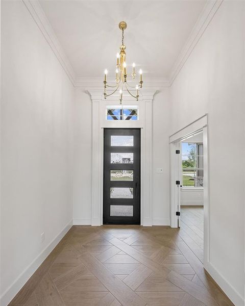 Foyer featuring a brass chandelier, wood-finish flooring with a geometric pattern, and a black multi-paneled door with transom window