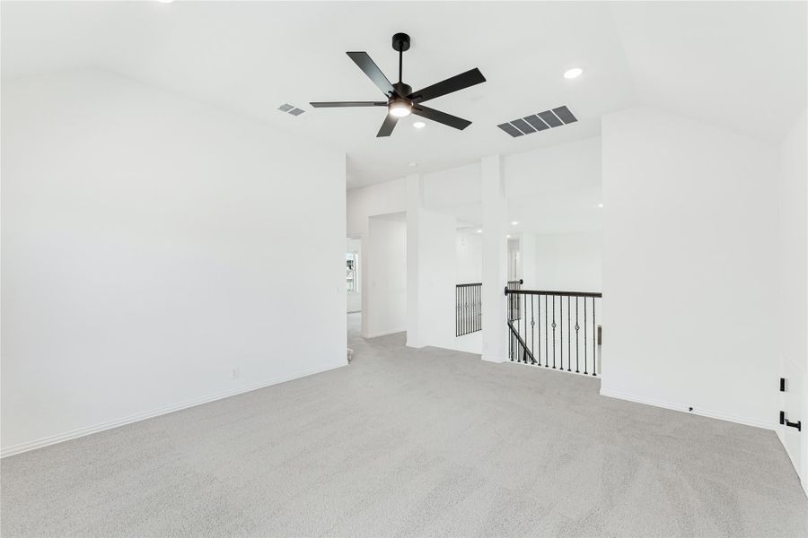 Open upstairs loft with gray carpet, black ceiling fan, and iron stair railing