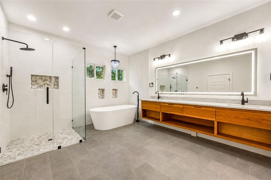 Luxurious Primary bathroom featuring a spacious glass-enclosed shower, freestanding tub, and elegant double vanity with ample storage and modern lighting.