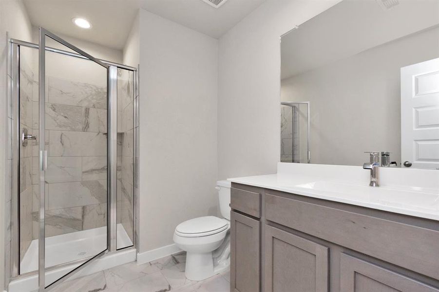 Experience sophistication in the guest suite bathroom, where tile flooring complements a walk-in shower with tile surround. Slate wood cabinets complete with a beautiful light countertop, enhances the space for a truly inviting ambiance. Sample photo of completed home with similar floor plan. As-built interior colors and selections may vary.