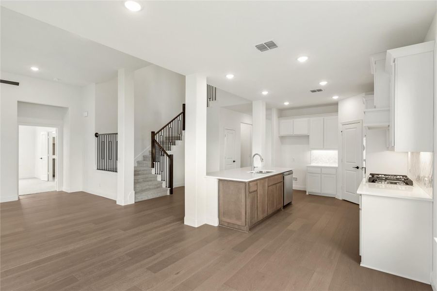 Open-concept kitchen with wood island, white cabinets, and hardwood floors, open to living area with staircase. Open-concept kitchen with wood island, white cabinets, and hardwood floors, open to living area with staircase.