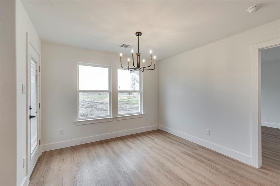 Empty room with light wood-style floors, visible vents, a chandelier, and baseboards