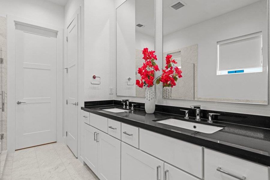 Double vanity with sleek dark countertops and modern fixtures anchors this bright primary bathroom. Double vanity with sleek dark countertops and modern fixtures anchors this bright primary bathroom.