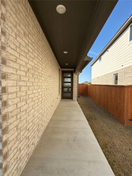 Covered entry featuring a modern dark-framed door with frosted glass panels, recessed lighting, and a light-toned brick facade