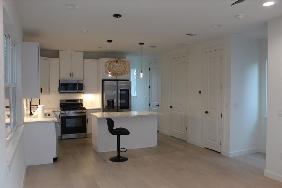 A streamlined kitchen flows into the main living area, featuring bright cabinetry, quartz countertops, and modern stainless steel appliances.