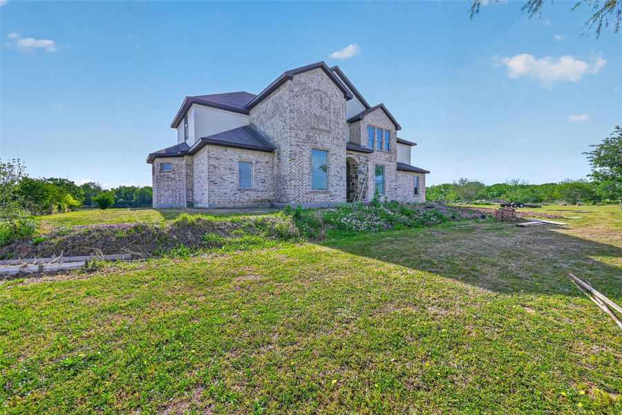 Angled front exterior view of Property 1 unfinished residence showcasing the scale of the structure, surrounding open space, and existing lawn.