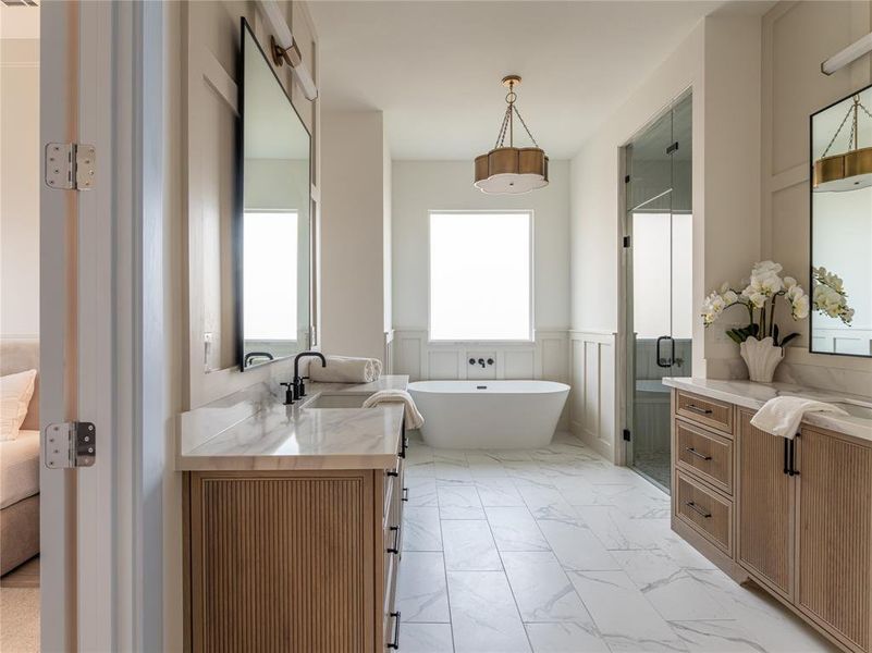 Full bathroom featuring two vanities, a wainscoted wall, a soaking tub, a stall shower, and ensuite bath