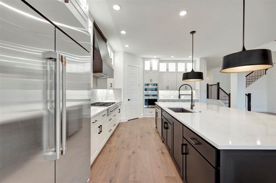 Dual tone kitchen with stainless steel appliances, dual tone cabinetry, hanging light fixtures, a large island, and light wood-style flooring