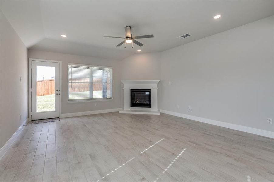 Spacious living area featuring light-toned wood-finish flooring, a white mantel fireplace, and recessed lighting