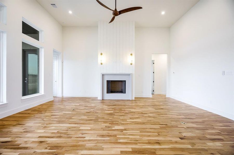 Unfurnished living room featuring ceiling fan, light hardwood / wood-style flooring, and a towering ceiling