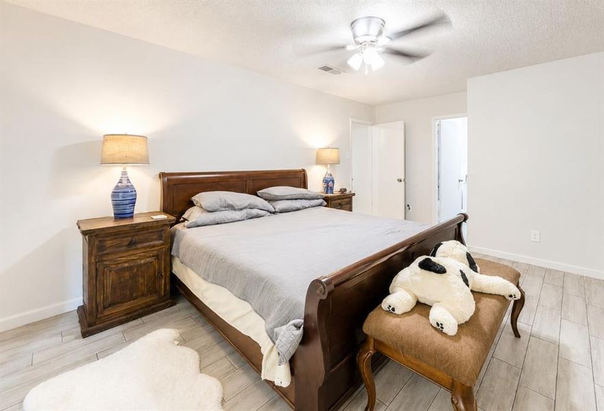Spacious bedroom featuring light-toned wood-finish flooring, a contemporary ceiling fan, and crisp white walls