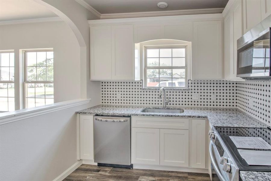 Kitchen with dark  crown molding, tasteful backsplash, stainless steel appliances, and sink