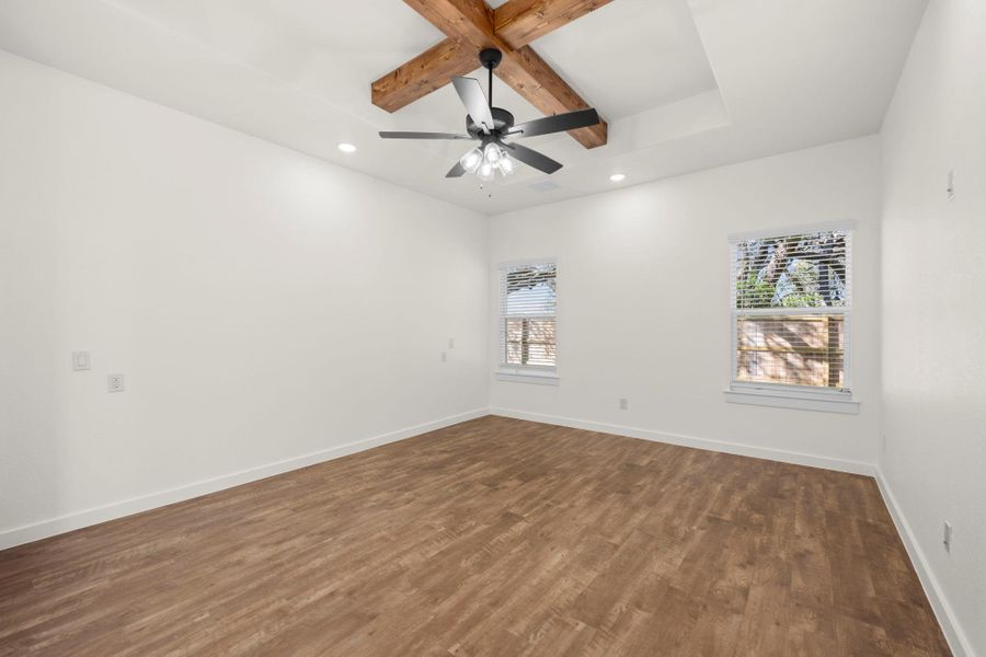 A spacious bedroom features striking wood beam accents on the ceiling and abundant natural light from dual windows.