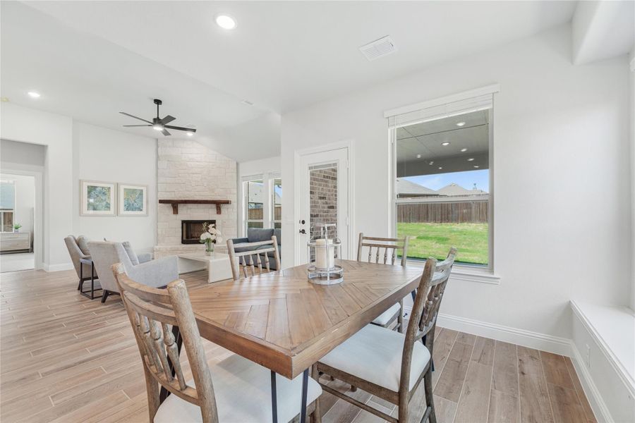 Dining area with wood table, open to living room with stone fireplace and ceiling fan Dining area with wood table, open to living room with stone fireplace and ceiling fan