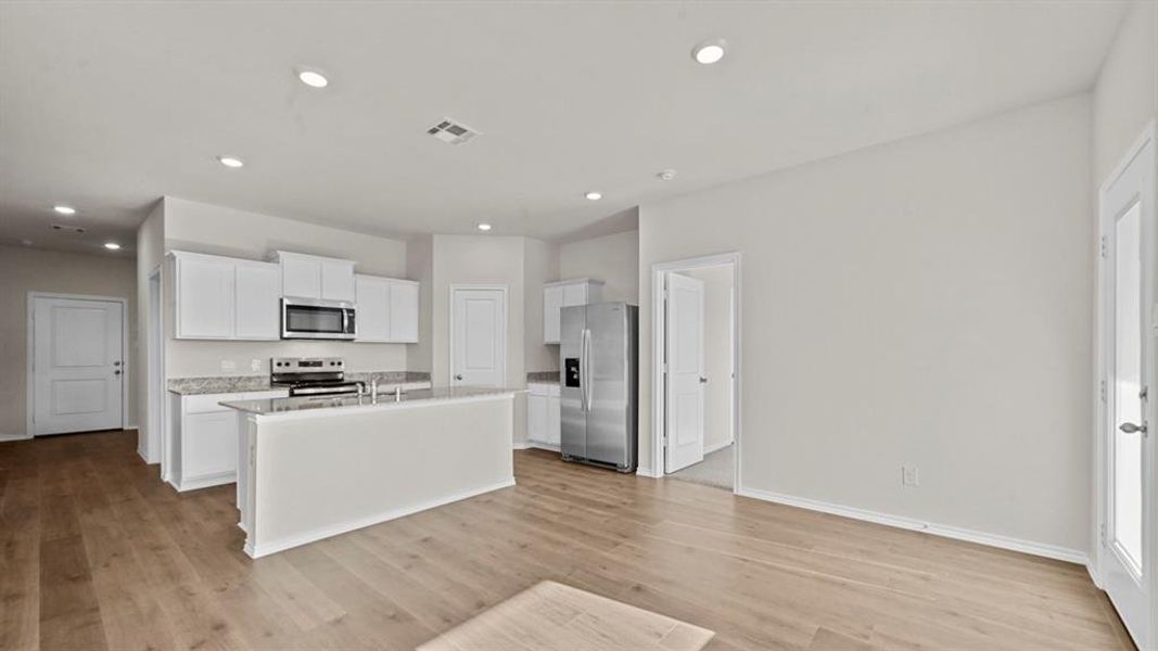 Kitchen featuring stainless steel appliances, white cabinets, an island with sink, light wood-type flooring, and open floor plan