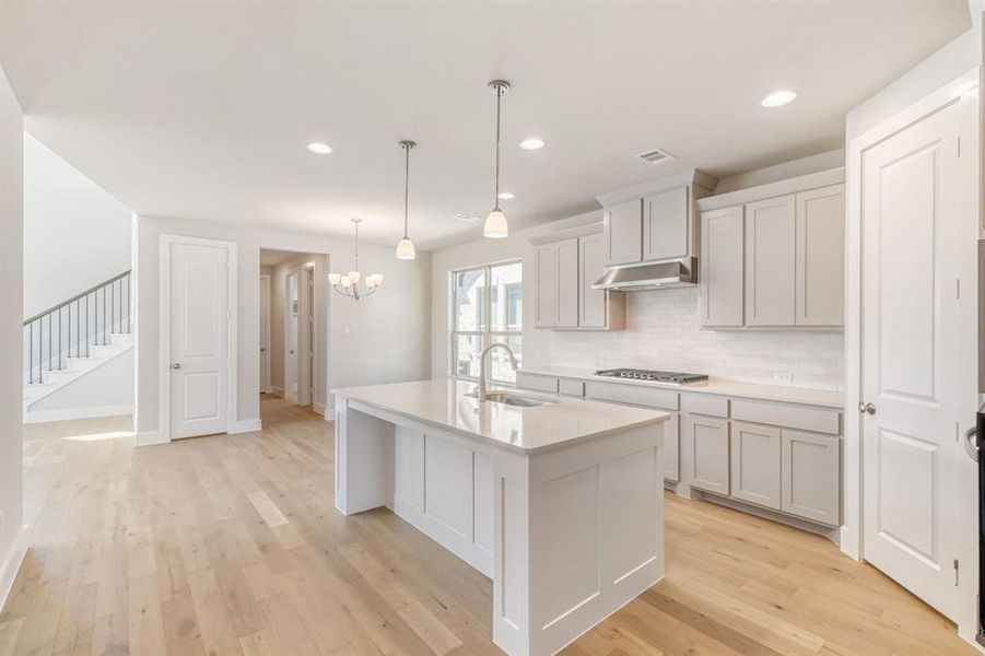Kitchen featuring a kitchen island with sink, tasteful backsplash, light wood finished floors, and light stone counters