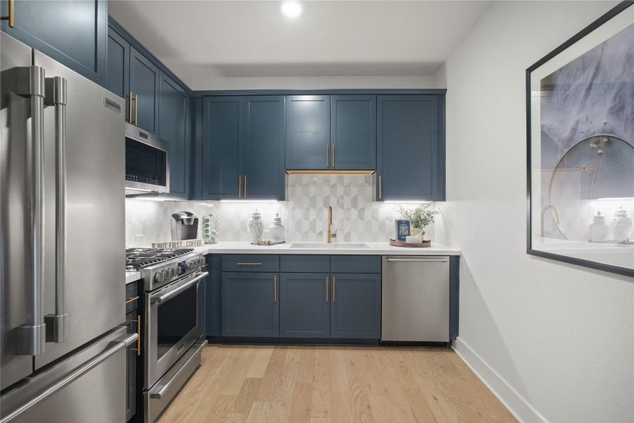 Caterers Kitchen with appliances with stainless steel finishes, backsplash, blue cabinetry, and light wood-style floors