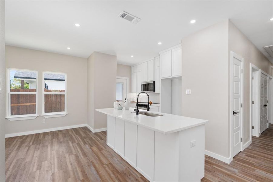 Kitchen featuring white cabinetry, light wood finished floors, recessed lighting, a center island with sink, and light stone countertops