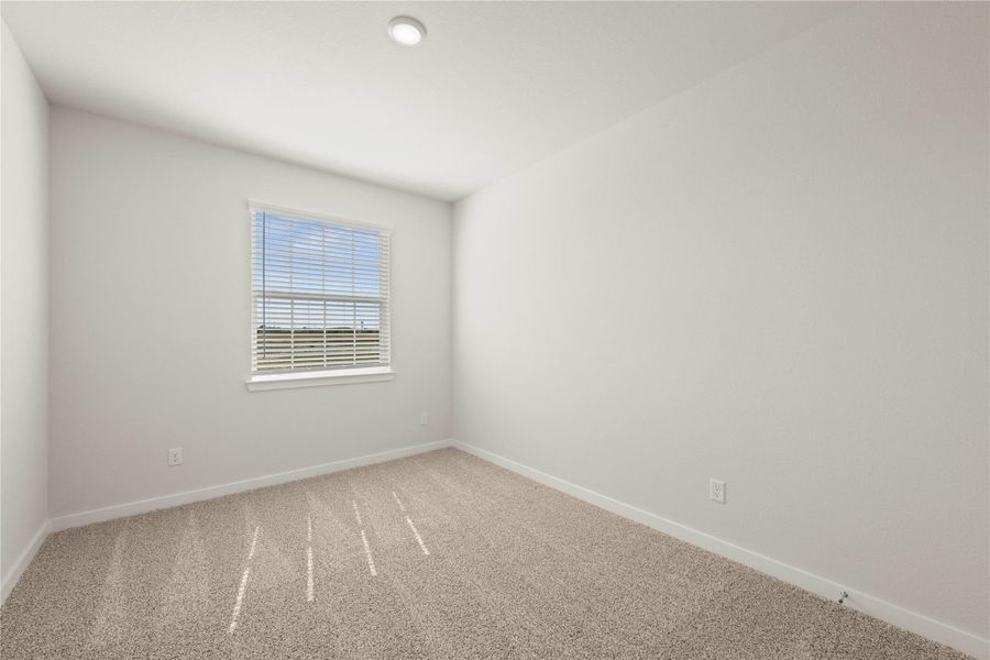 A well-lit, neutral-toned room features a large window with blinds and soft carpeting.