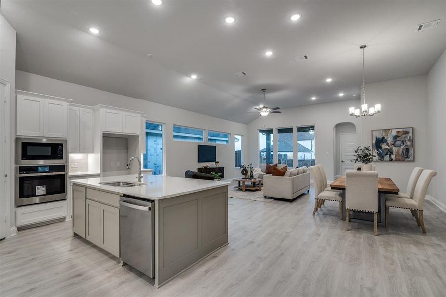 Kitchen featuring sink, a center island with sink, white cabinets, ceiling fan with notable chandelier, and appliances with stainless steel finishes