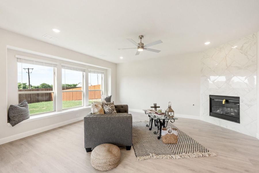 Living room with white tile fireplace, ceiling fan, window seat, and light hardwood floors