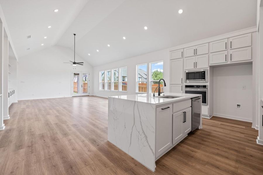 Kitchen featuring white cabinetry, high vaulted ceiling, light stone countertops, a kitchen island with sink, and light wood-type flooring Kitchen featuring white cabinetry, high vaulted ceiling, light stone countertops, a kitchen island with sink, and light wood-type flooring