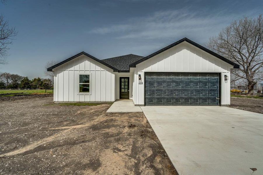 Modern inspired farmhouse with an attached garage, concrete driveway, board and batten siding, and roof with shingles