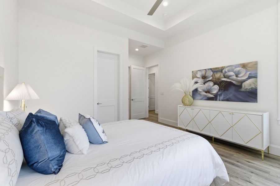 Bedroom with light wood-type flooring, ceiling fan, recessed lighting, and a tray ceiling