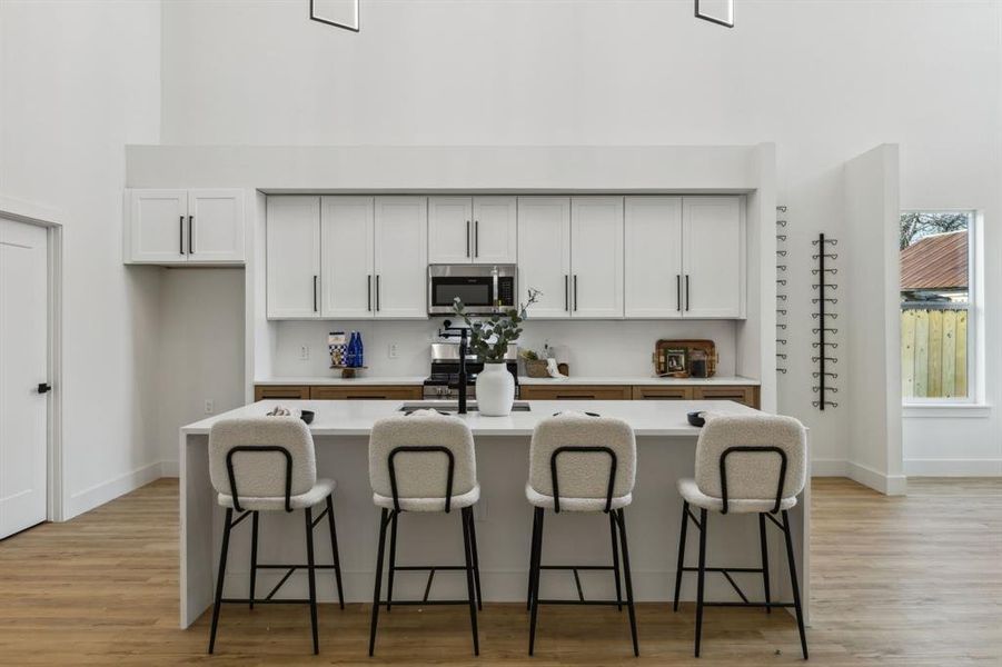 Kitchen with light hardwood / wood-style floors, white cabinets, a breakfast bar area, and an island with sink