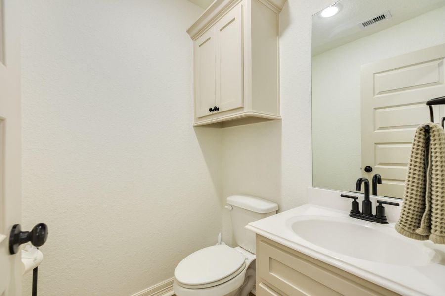 This is a well-lit bathroom with a modern white vanity and black fixtures. It features a toilet, a large mirror, and a cabinet for storage.