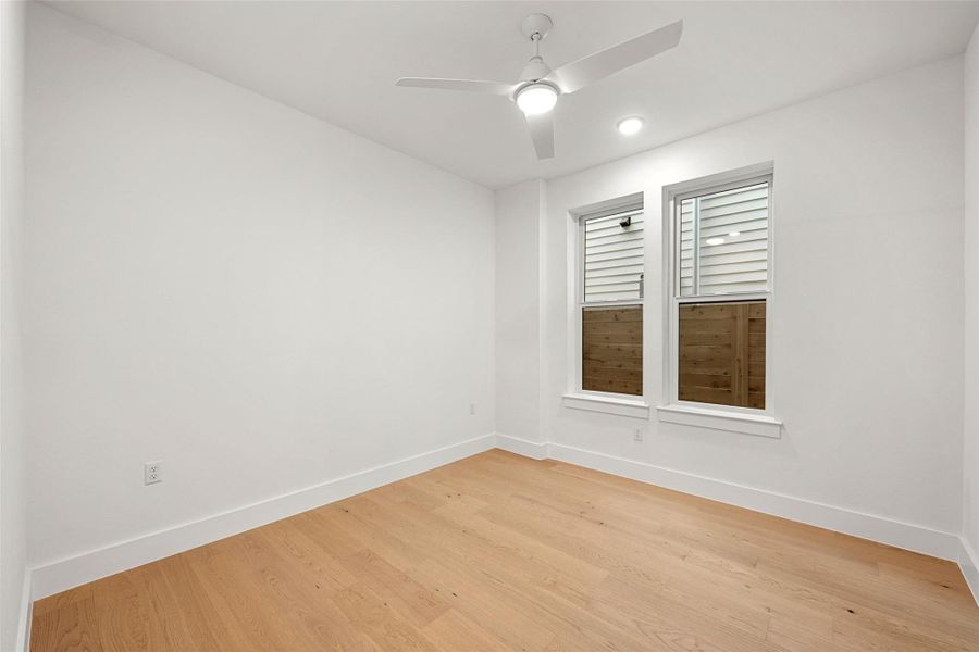 A quiet bedroom showcases light wood flooring and a modern ceiling fan, offering a serene retreat. A quiet bedroom showcases light wood flooring and a modern ceiling fan, offering a serene retreat.
