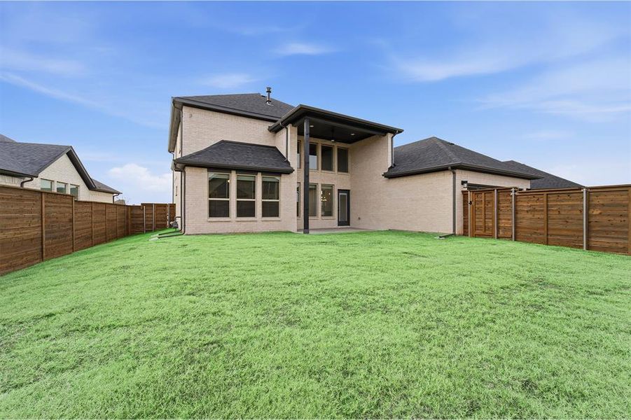 Expansive backyard featuring a manicured lawn, complete wood fencing, and a covered patio with direct house access