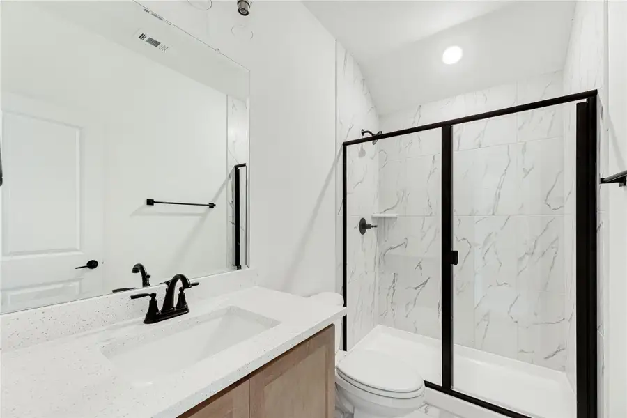 Bathroom with quartz vanity, black fixtures, and glass-enclosed shower with marble-look tile walls