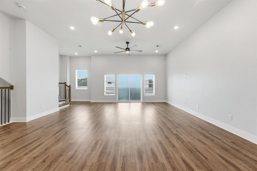 Expansive open living area featuring wide-plank flooring, modern chandelier, recessed lighting, and abundant natural light with access to a private balcony.